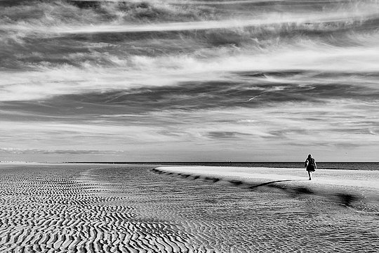 Person geht allein über eine Sandbank am Meer.