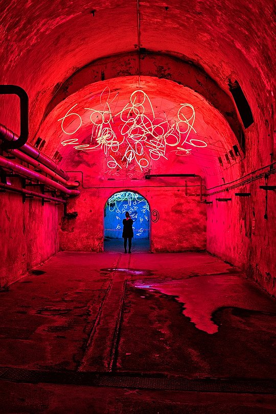 Person steht in einem rot beleuchteten Tunnel mit Lichtinstallation / Lichtmalerei