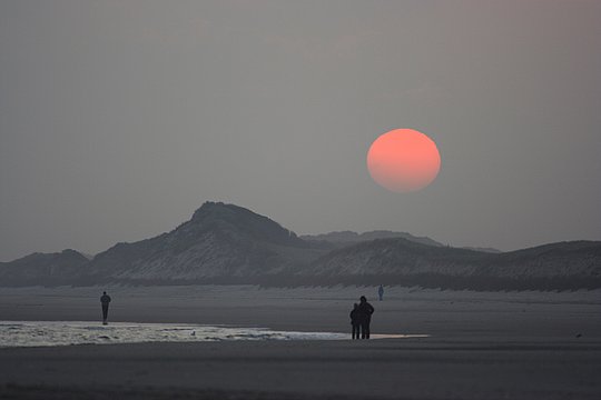 Sonne über einem nebligen Strand mit mehreren Personen.