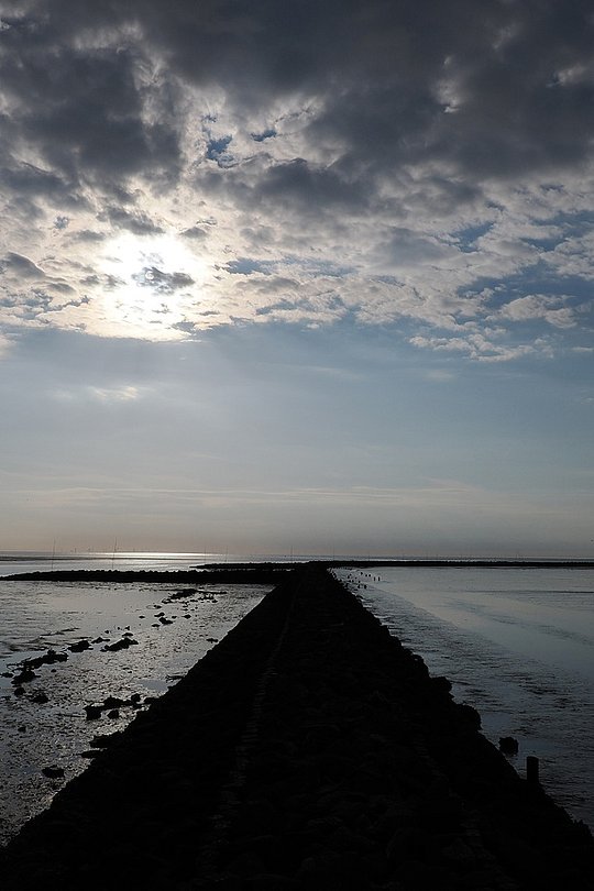 Schmaler Damm führt durch flaches Wasser zum Horizont.