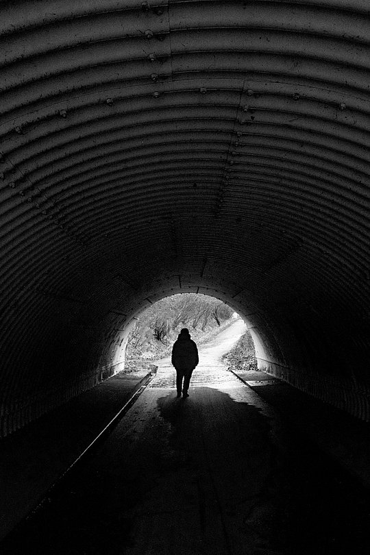 Person als Silhouette geht durch einen dunklen Tunnel ins Licht.