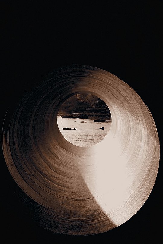 Blick durch ein rundes Rohr auf eine Wasserfläche im Licht.