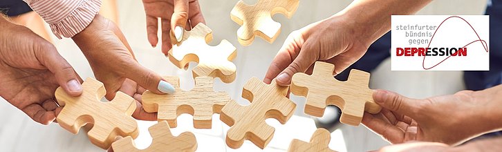 mehrere Hände fürgen symbolisch Holzpuzzleteile zusammen