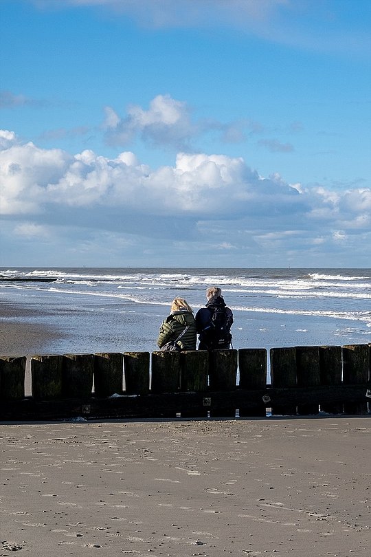Zwei Personen sitzen am Strand und blicken aufs Meer.