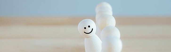 Reihe Spielfiguren, eine hat ein Smiley aufgemalt und schaut aus der Reihe